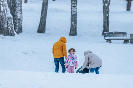 Valmiera, Latvia - January 11, 2026: Family is having fun in snowy park, child is playing in snow while parents help, creating a joyful atmosphereのeditorial素材