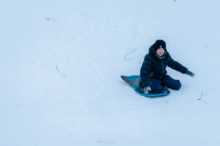 Valmiera, Latvia - January 11, 2026: Young boy wearing winter gear is sledding down snowy slope, experiencing excitement and fun in a winter wonderlandのeditorial素材