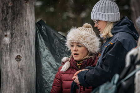 Ligatne, Latvia - January 11, 2026: Two women dressed in warm winter attire are talking outdoors amidst snow-covered trees, creating a cozy winter sceneのeditorial素材