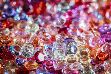 A vibrant collection of sparkling glass gems in various colors and shapes is scattered across a surface, creating an eye-catching decorative displayの写真素材
