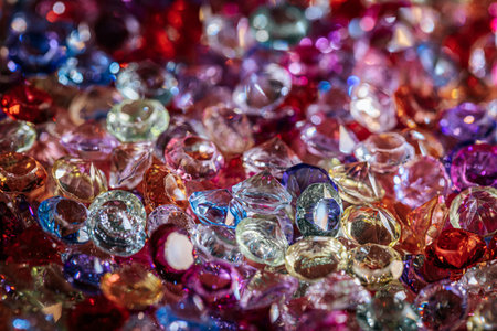 Assorted sparkling gemstones and crystals in various colors and shapes are scattered on a textured surface, reflecting light and creating a vibrant visual effectの写真素材