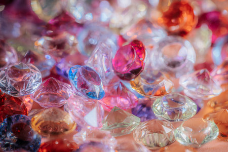 Assorted sparkling gemstones in various colors and shapes are scattered on a surface, highlighting...