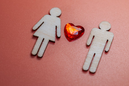 Wooden male and female figures with a red heart gem on a coral background, symbolizing love and relationships in a decorative arrangementの写真素材