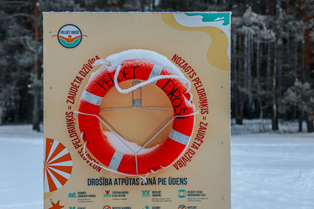 Valmiera, Latvia - January 21, 2026: Lifebuoy safety sign in Latvian language covered in snow, set...