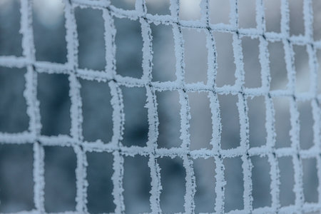 Close-up of a frost-covered net with ice crystals, set against a blurred winter background, highlighting the details of the frozen sceneの写真素材