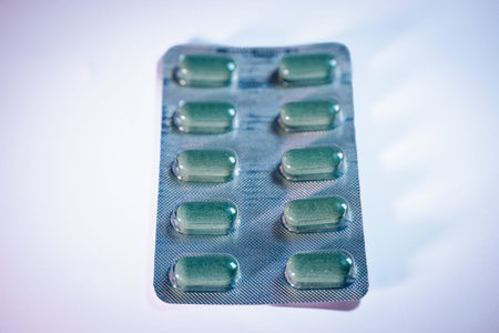 Blister pack features twelve green capsules in two rows, placed on a reflective surface with soft...