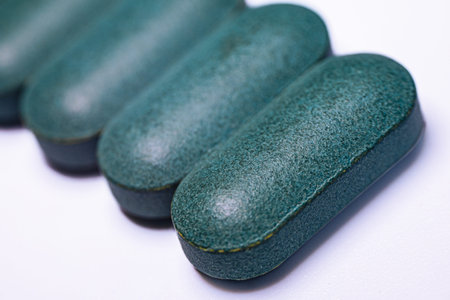 Green capsules lined up on a white background, highlighting their smooth surface and oval shape, suitable for health and wellness themesの写真素材