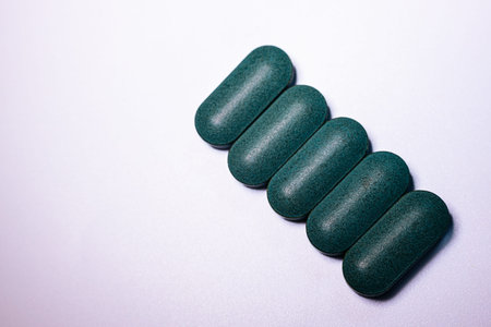 Green oval dietary supplements are neatly arranged in a row on a light background, highlighting...