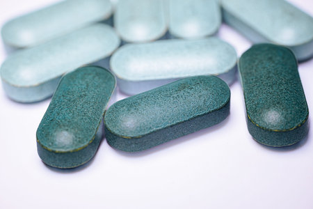 Teal oval tablets are displayed on a white background, highlighting their smooth surface and rounded...