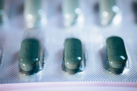 Green capsules are displayed in a blister pack, highlighting their smooth surface and distinct...