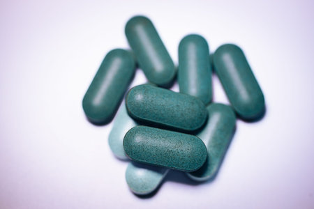 Green capsules of dietary supplements are stacked together on a light surface, displaying different shades and textures in a close-up arrangementの写真素材