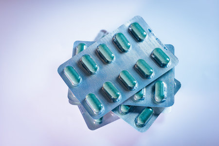 Stacked blister packs containing green capsules are displayed against a light background,...