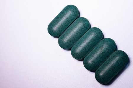Green dietary supplements displayed in a straight line on a white background, highlighting their oval shape and smooth surface for health-related usesの写真素材