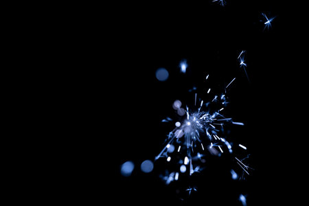 Blue sparkler produces bright light and shimmering particles against a black background, creating a visually striking effect in a dark environmentの写真素材