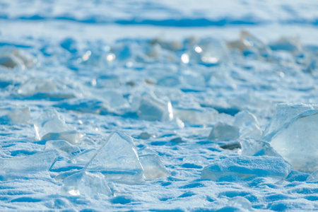 Ice pieces are spread across a snow-covered ground, reflecting sunlight and creating a shimmering...