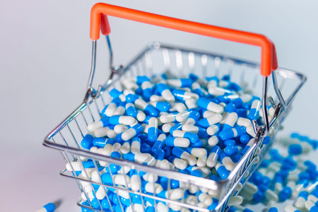 Shopping basket contains numerous blue and white capsules against a light background, highlighting different sizes and shapes of medicationの写真素材