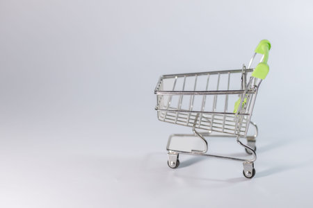 Metallic shopping cart with a green handle placed on a light gray background, ideal for retail or e-commerce imagery and product displaysの写真素材