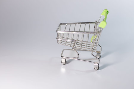 Small metallic shopping cart with a green handle placed on a gray surface, emphasizing a sleek and modern design suitable for retail contextsの写真素材