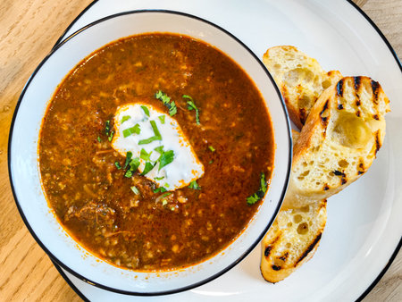 Bowl of hearty brown soup topped with herbs and cream, accompanied by grilled bread slices on a...