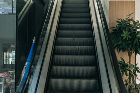 Escalator ascends in a contemporary shopping mall, featuring glass walls and green indoor plants alongside the structureの写真素材