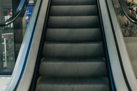 Close-up of escalator steps ascending in a contemporary shopping mall, featuring glass walls and greenery in the backgroundの写真素材