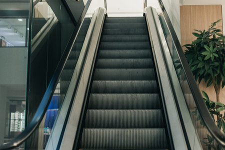 Escalator ascends in a contemporary building, featuring glass railings and indoor plants, highlighting modern architectural design and interior elementsの写真素材