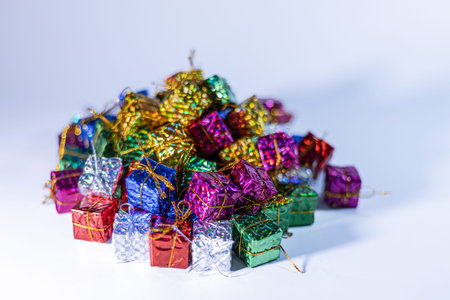 Miniature gift boxes in vibrant metallic colors are piled together on a white background, suitable...