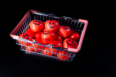 Shopping basket contains multiple red balls featuring smiley face designs, set against a solid black...