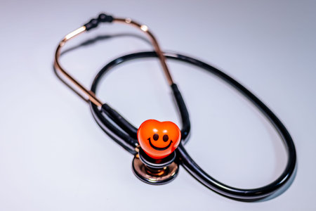 Stethoscope featuring an orange heart-shaped smiley face attachment placed on a white background,...
