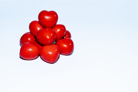 Red heart-shaped decorations are stacked in a pyramid shape against a light blue background,...