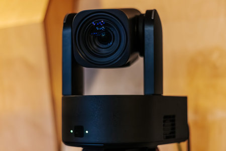 High-definition video camera with a rotating lens positioned on a tripod, featuring a wooden wall...