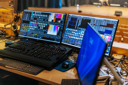Dual monitors display lighting control software on a wooden desk in a performance venue, with...