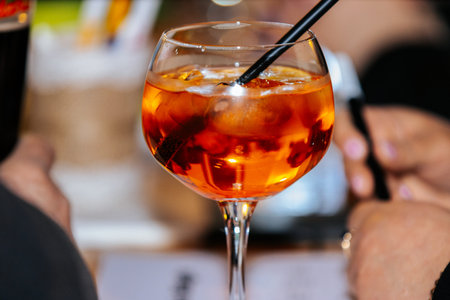 Valmiera, Latvia - March 06, 2026: Close-up view of a cocktail glass containing an orange beverage with ice cubes and a black straw in a bar environmentのeditorial素材