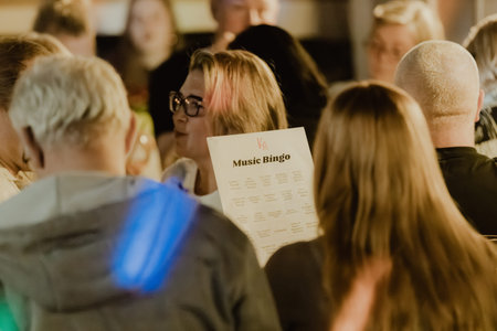 Valmiera, Latvia - March 06, 2026: People engaged in a Music Bingo event, with a woman in glasses...