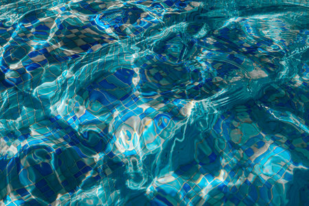 Clear water in a swimming pool reflects sunlight, creating ripples and patterns, with colorful...