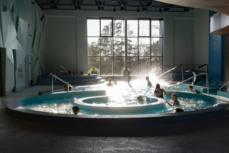 Indoor pool area with several hot tubs and people relaxing in the water, large windows providing...