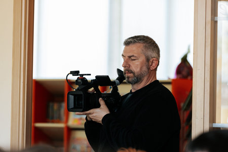Valmiera, Latvia - March 17, 2026: Male videographer with a gray beard holds a camera in a well-lit...