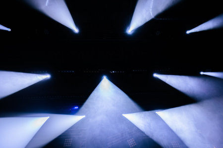 Bright stage lights project beams through fog in a concert environment, creating a striking visual effect in the dark setting