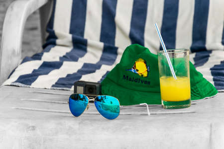 Summer holiday abstract with a green hat, blue sunglases and orange juice lying on a black-white beach chair, just like dreaming of a summer holiday.の写真素材
