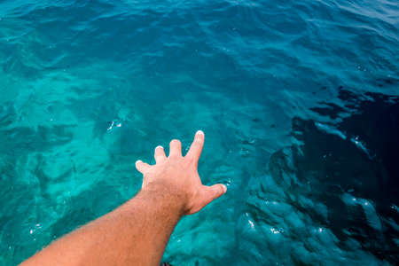 Hand of a young caucasian male Appearing to touch the surface of amazing blue water of the Indian Ocean.の写真素材