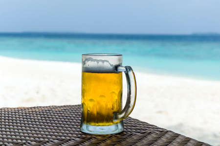 Beer mug lying on a table in front of white sand beach and turquoise colored ocean in Maldives.の写真素材