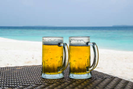 Beer mug lying on a table in front of white sand beach and turquoise colored ocean in Maldives.の写真素材
