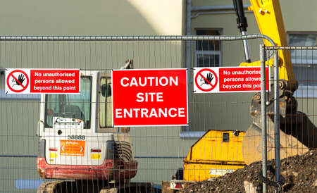 Caution sign at entrance to construction site.Red plaque hanging on the fence in the middle between...