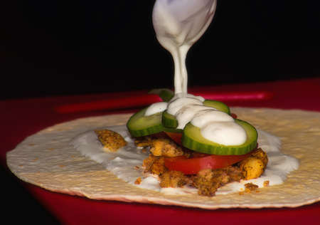 Preparation of tortillas with chunks of chicken and vegetables, flooding garlic sauceの写真素材