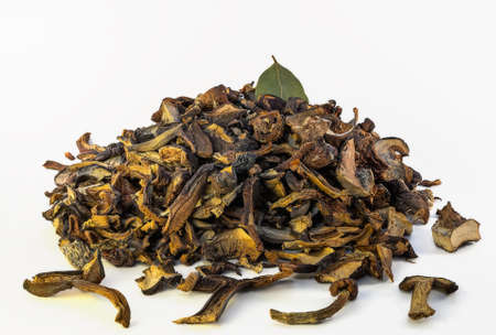 A pile of dried wild mushrooms with bay leaves on top on a white background.の写真素材
