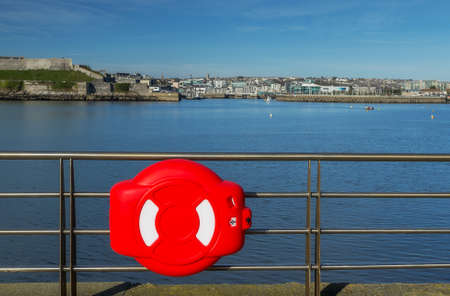 Lifebuoy enclosed in plastic cover hanging on the pier in Plymouth, UK.