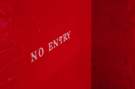 White NO ENTRY inscription on a brick wall painted red.