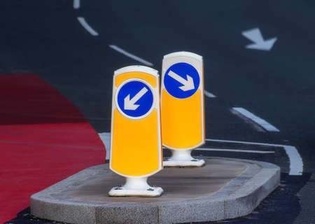 Road safety directional arrow on illuminating bollard standing in the middle of a winding colorful road.の写真素材