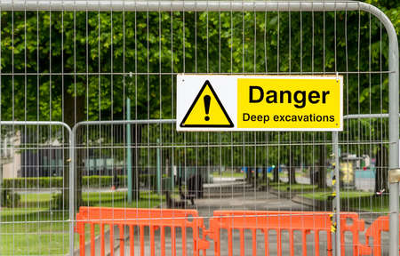 Yellow warning sign with an exclamation mark hung on the fence repaired pavement.の写真素材