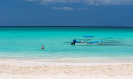 Boy next to passenger boat moored at the shore of the Dominican island of Saona.
